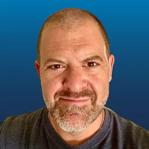 An image of Loren Weisman with a blue background. He is wearing a gray tee shirt and has very short hair and a short beard.